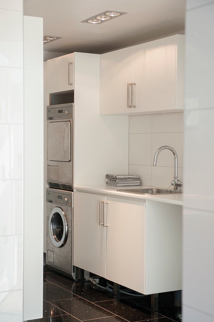 Blick in Waschraum auf Spültisch neben Schrankkorpus mit integrierter Waschmaschine und Trockner