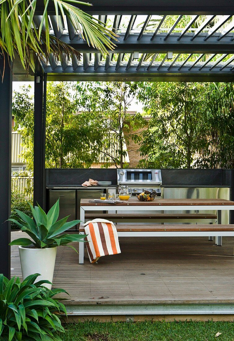 Moderne Terrasse mit Tisch- und Bankgarnitur unter Pergola mit Lamellen Abdeckung