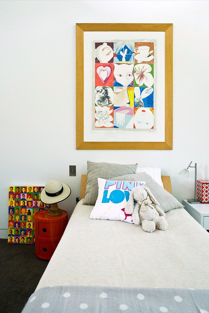 Scatter cushions and cloth rabbit on child's bed below framed picture