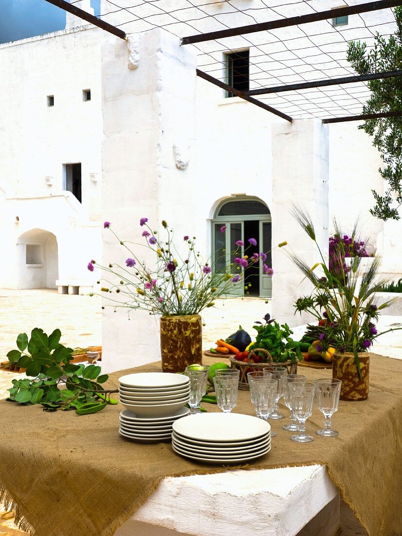 Tisch mit ockerbrauner Tischdecke, Geschirr und mediterranen Blumensträussen, im Freien unter Pergola