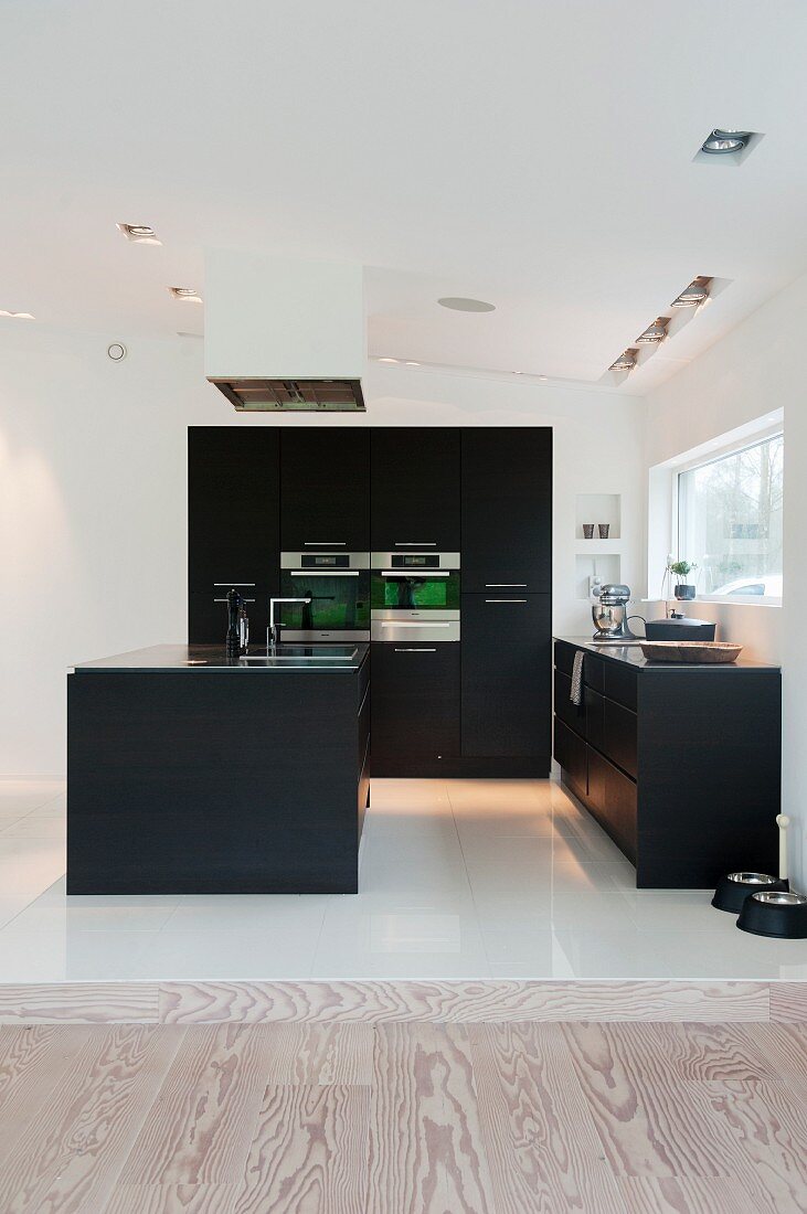 Black designer kitchen with white floor tiles in open-plan interior