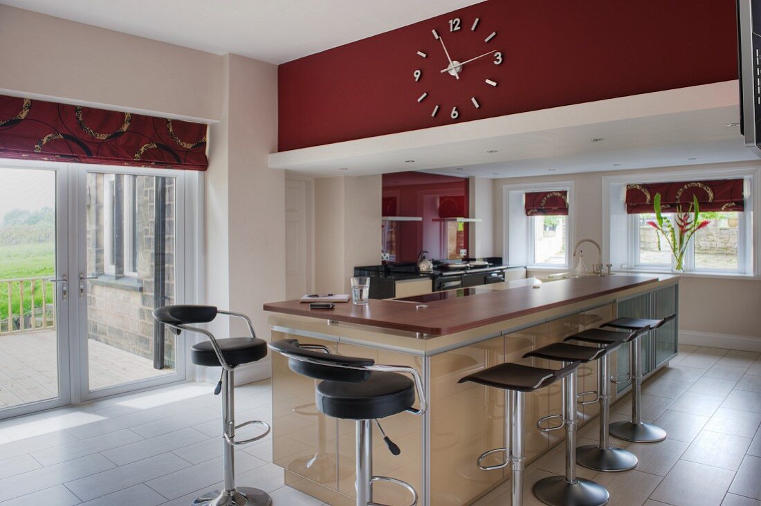 Island counter with red Corian worksurface and bar stools with black seas in open-plan kitchen