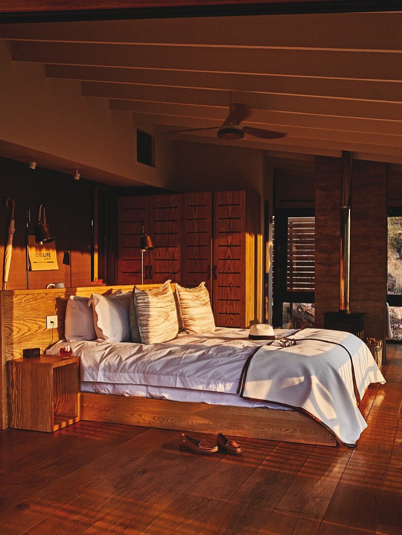 Doppelbett mit Holzrahmen und Betthaupt im Sonnenlicht, in Schlafzimmer mit Brauntönen