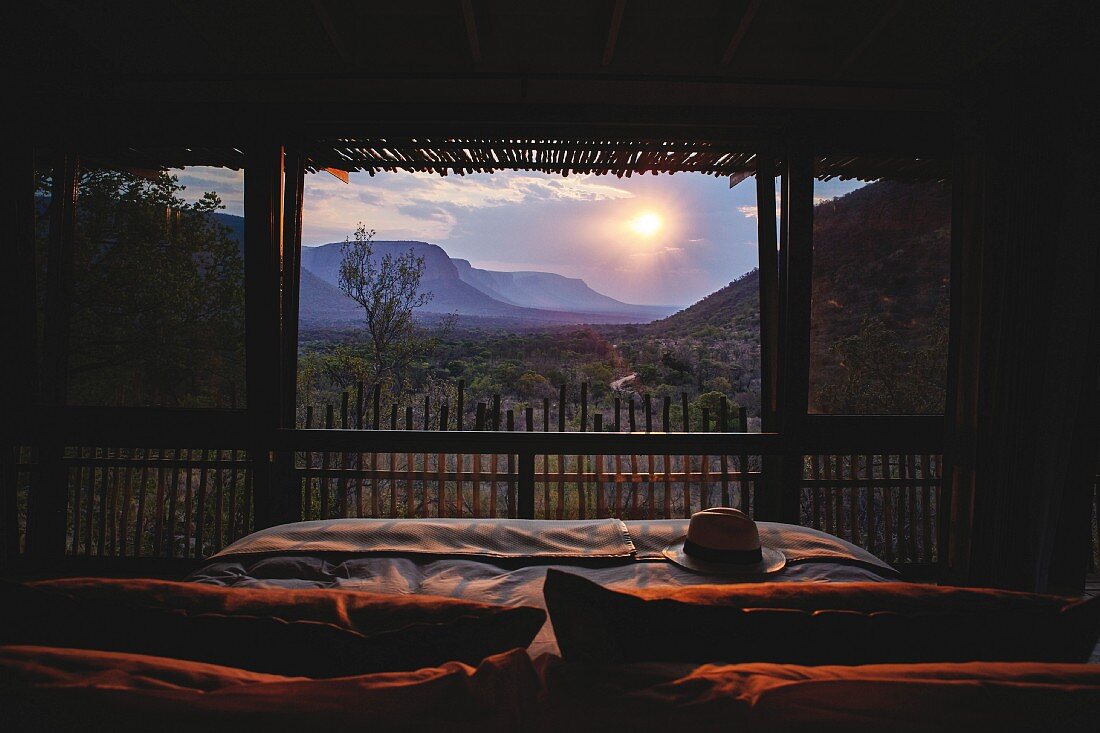 Romantic view of sunset over wild landscape seen from bed through panoramic window
