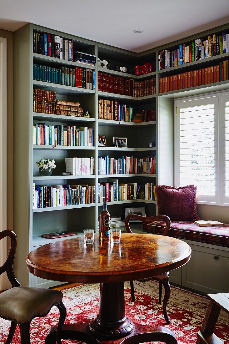 Round table and antique-style chairs in front of fitted bookcases and custom window seat