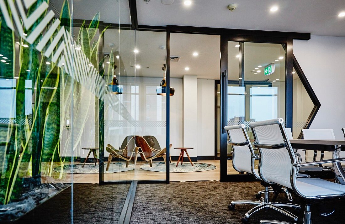 Klassiker Bürostühle in modernem Büro, im Hintergrund Stahl-Glaswand mit offener Tür und Blick in Loungebereich