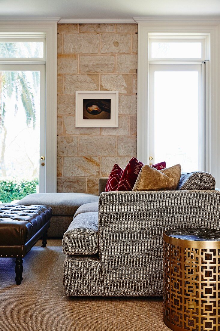 Grey sofa and brass side table with geometric perforated pattern in traditional living room with stone wall