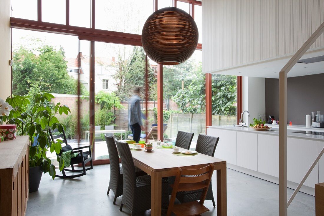 Essplatz mit Rattanstühlen in offener Küche in einem Loft, im Hintergrund Mann auf Terrasse