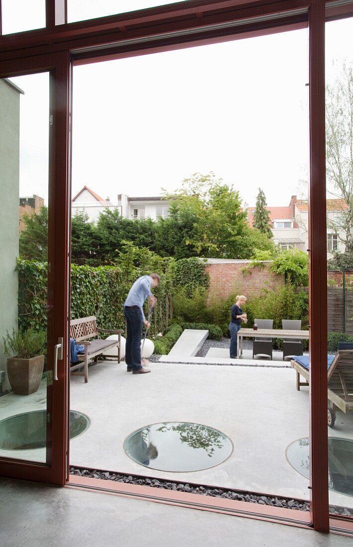 Blick auf Terrasse, kreisförmige Ausschnitte mit Glasbelag im Betonboden, im Hintergrund Mann und Frau