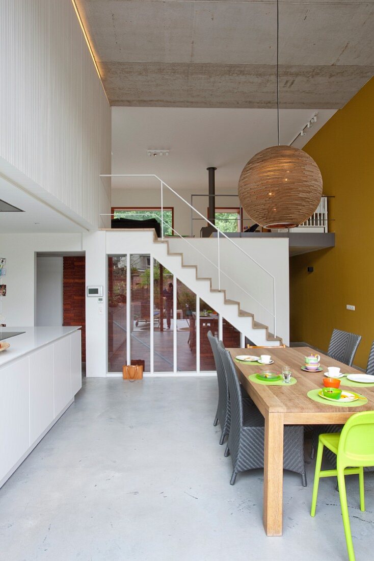 Wicker chairs and green highchair at wooden table: staircase and gallery in background in contemporary loft apartment