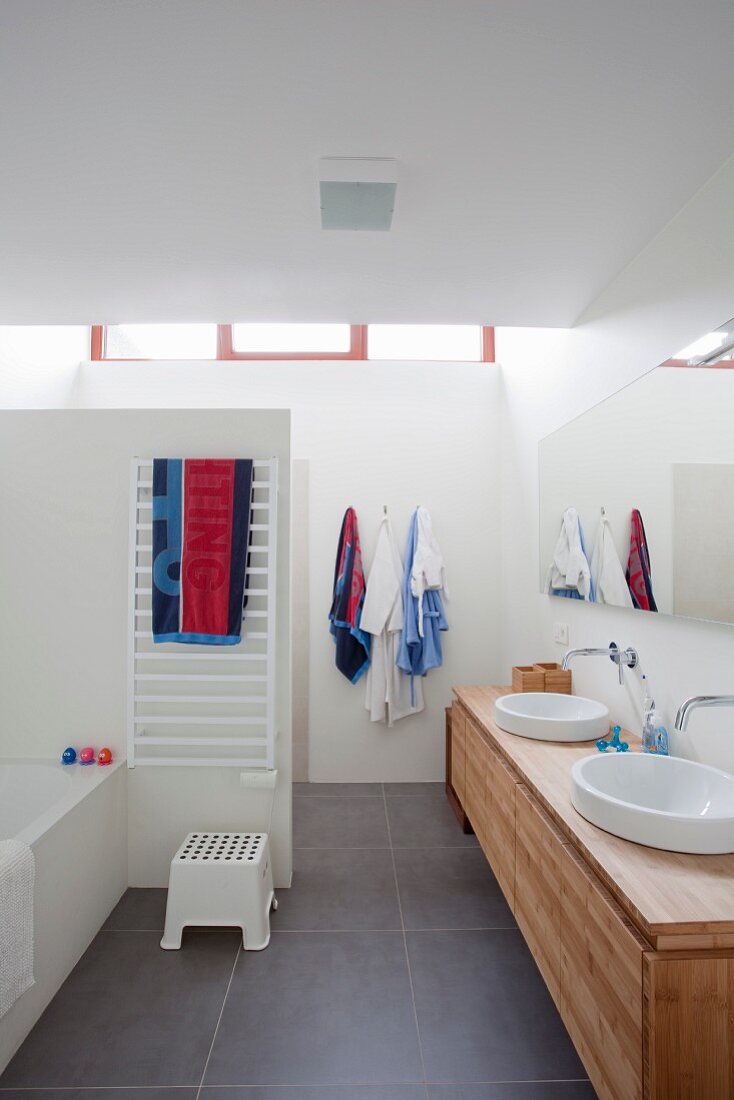 Waschtischzeile mit Aufbaubecken auf Holz Unterschrank, im Hintergrund abgetrennter Duschbereich in modernem Bad mit grauen Fliesenboden