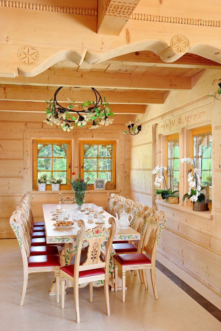 Bemalte Holzstühle mit Schnitzereien um Esstisch in Zimmerecke in einem Massivholzhaus