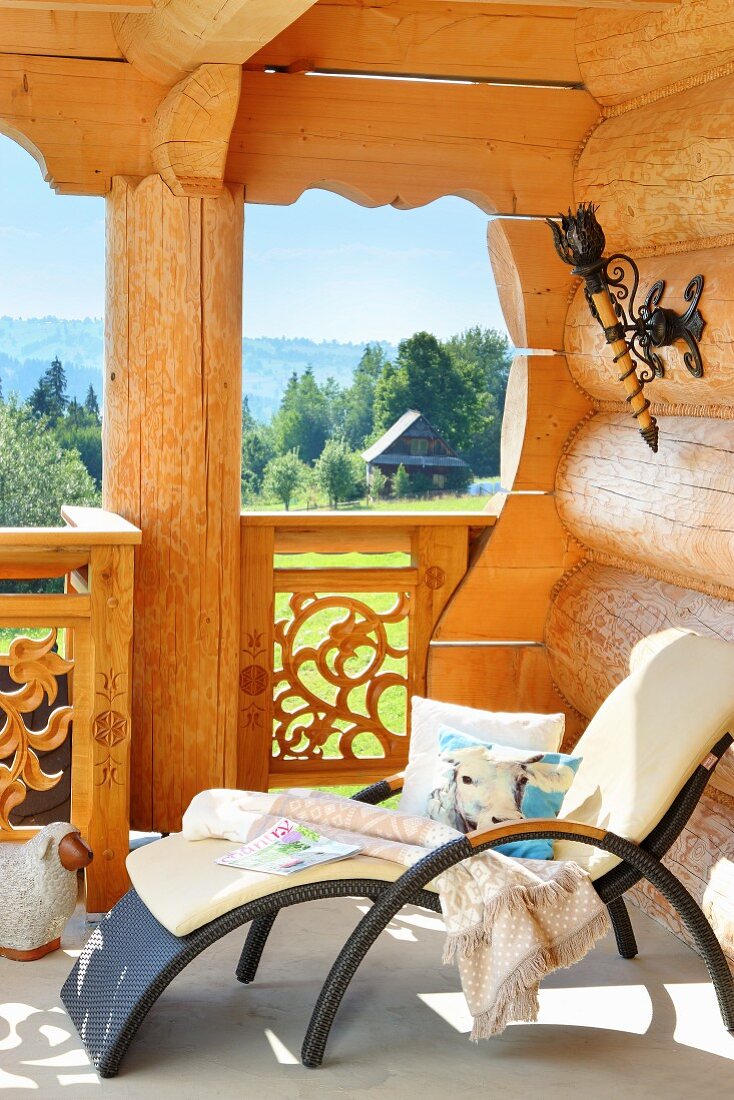 Modern outdoor lounger with white cushions on balcony of log cabin with view of idyllic landscape