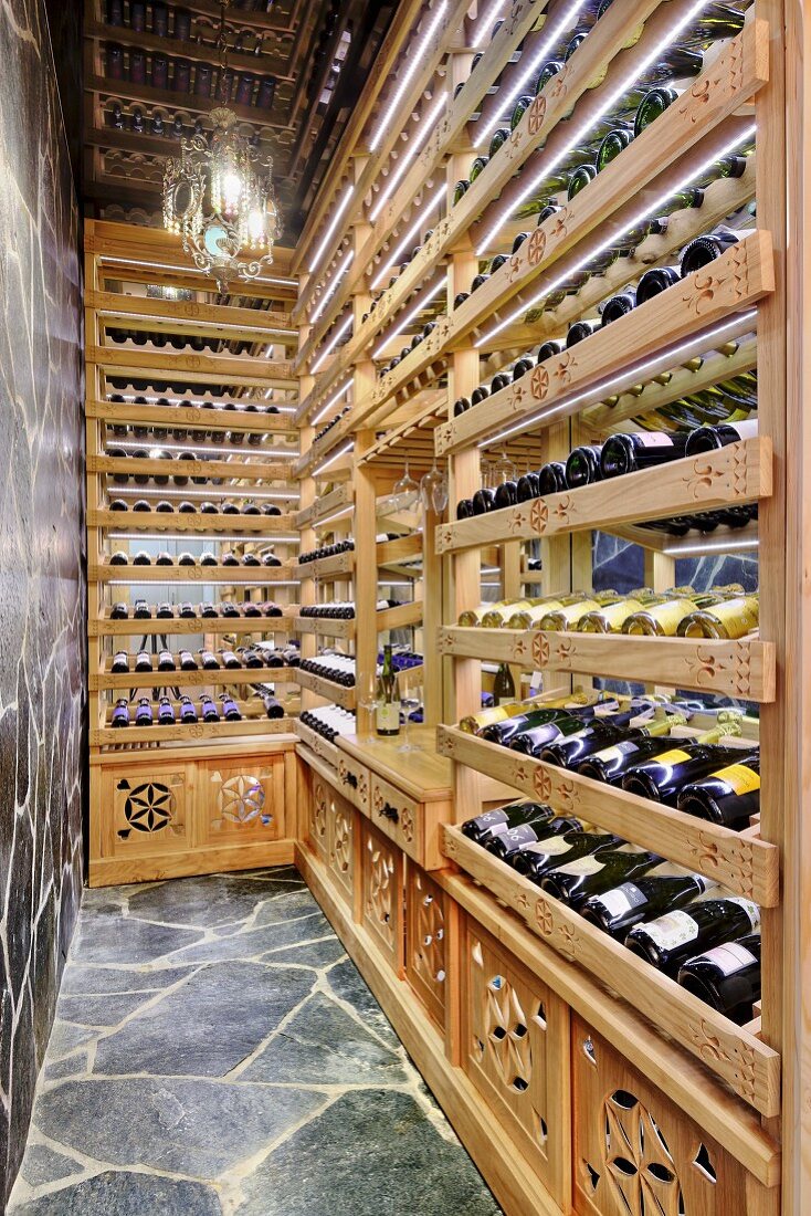 Pale wooden wine racks in narrow room with stone-clad wall and floor