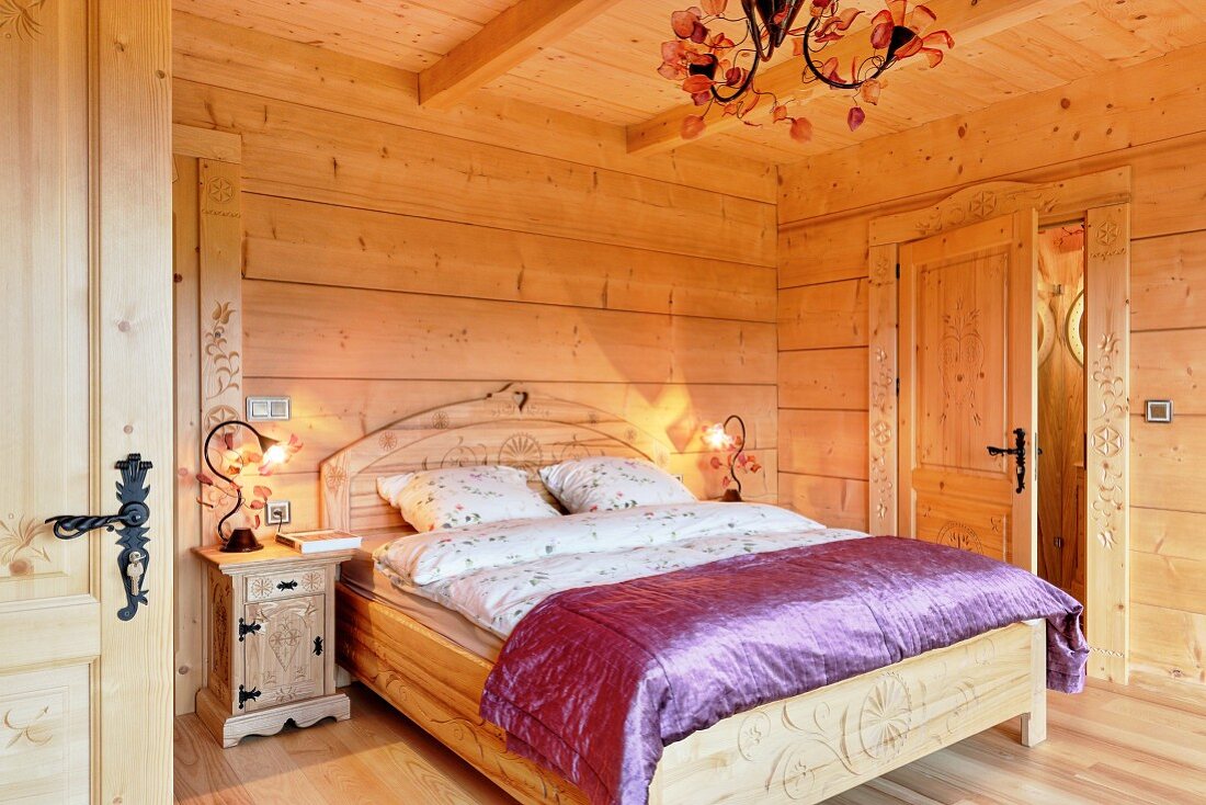 Doppelbett mit geschwungenem Kopfteil und violetter Seidendecke im Massivholzhaus