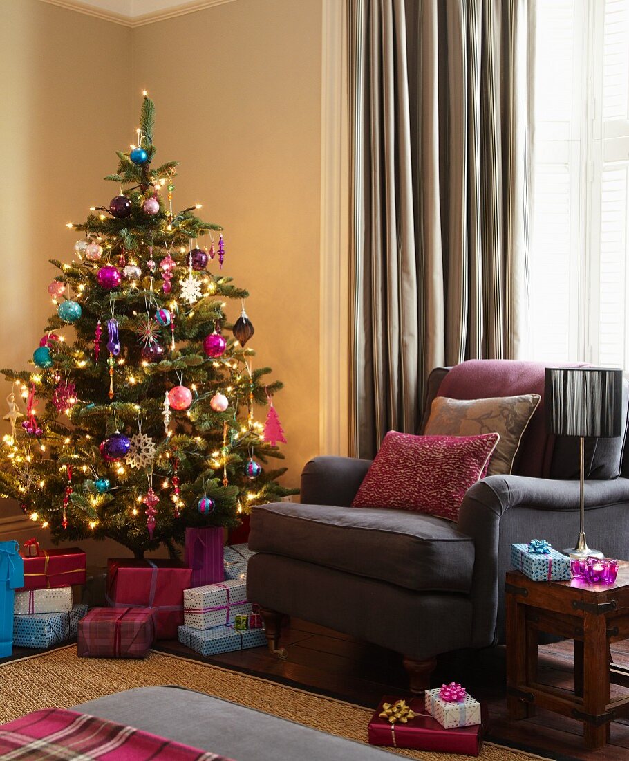 Decorated Christmas tree and presents next to brown armchair in corner of living room