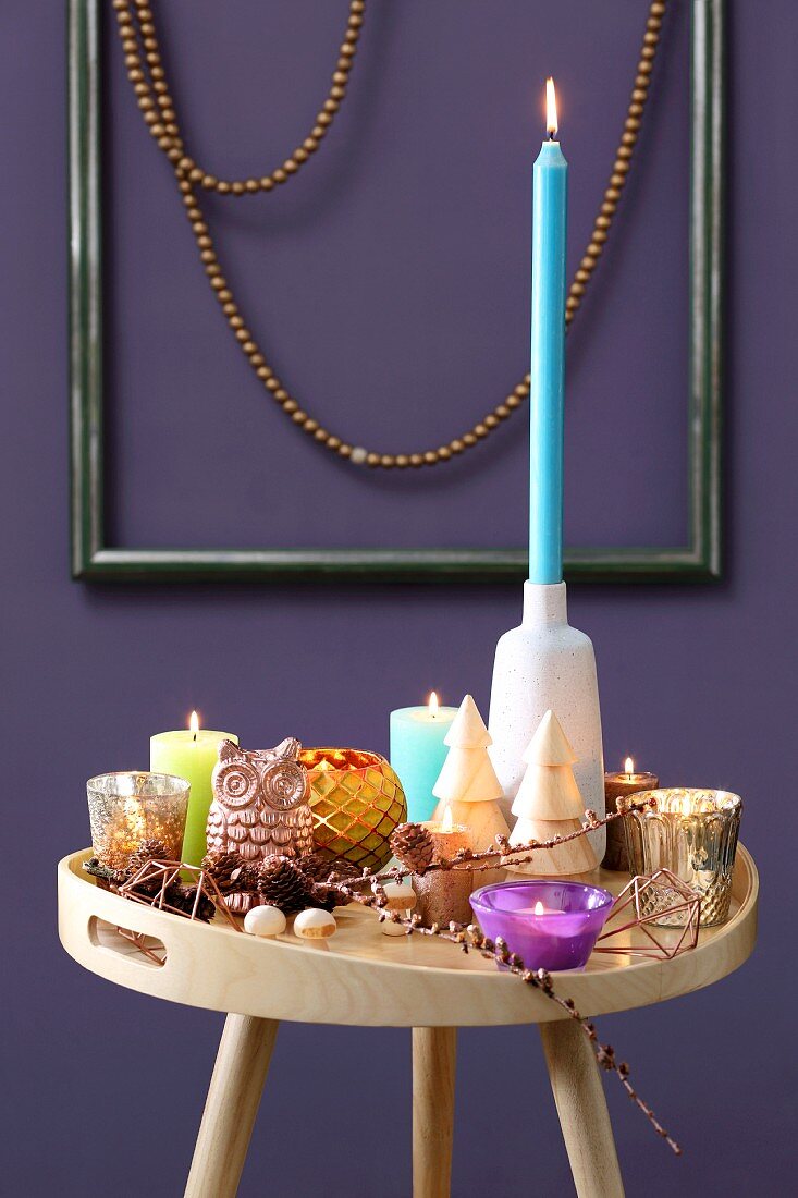Tabletttisch mit bunter Kerzendeko vor lila Wand