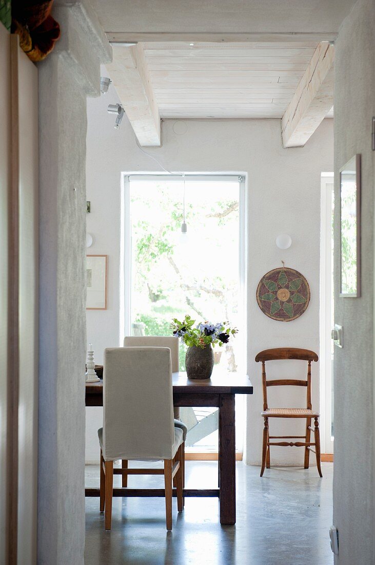 Dining area with pale upholstered chairs and wooden chair between French windows in background