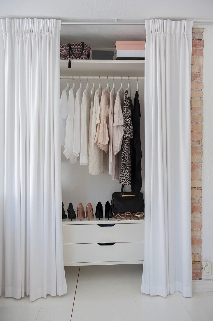 Offene, bodenlange weiße Vorhänge vor Kleiderschrank mit Blick auf Damenkleidung