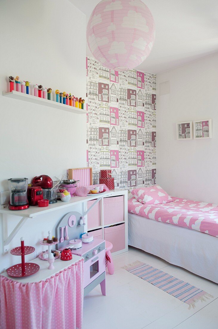 Mädchenzimmer mit rosa Farbakzenten, Kinderküche, Bett vor tapezierter Wand mit Häusermotiv