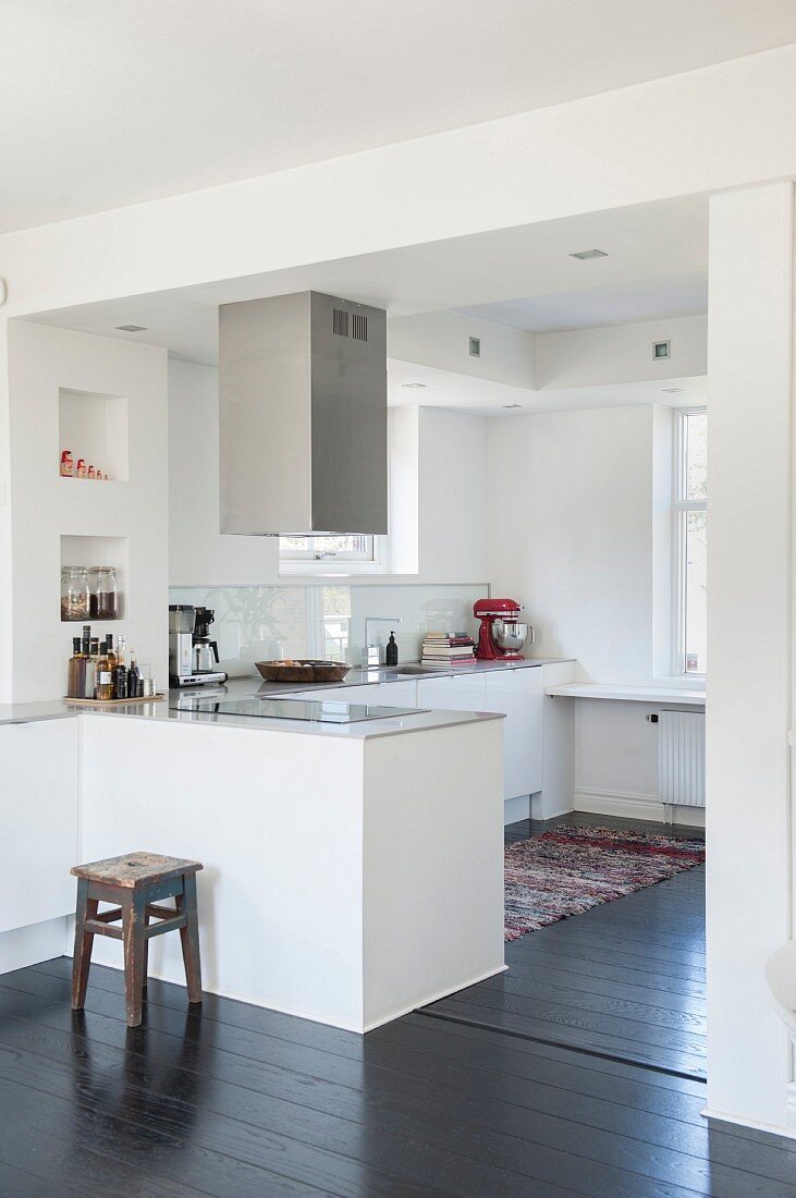 Open-plan white kitchen with counter and stainless steel extractor hood
