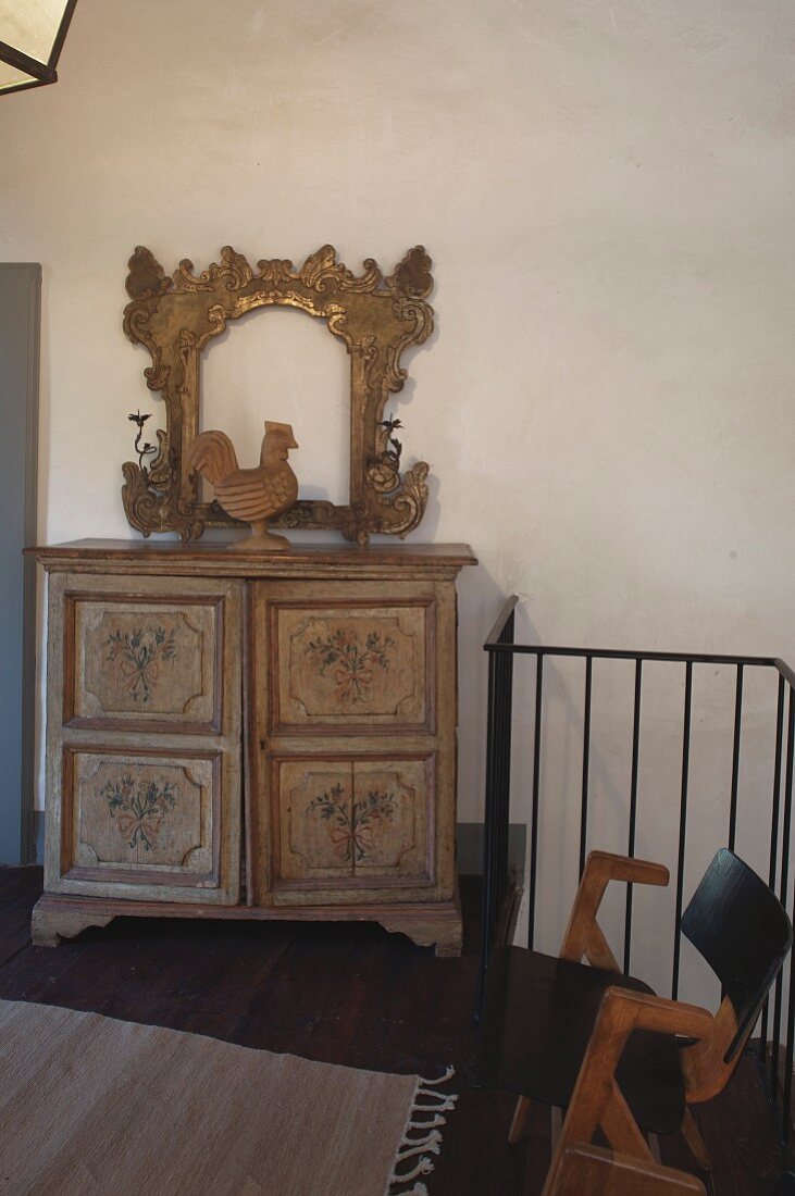 Carved cockerel and gilt frame on top of antique farmhouse cabinet on landing with balustrade