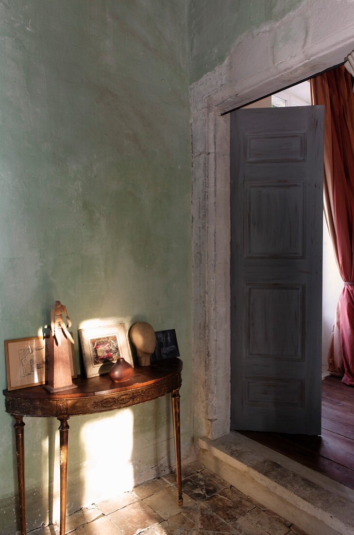 Delicate antique console table next to open double doors in rustic, Mediterranean interior