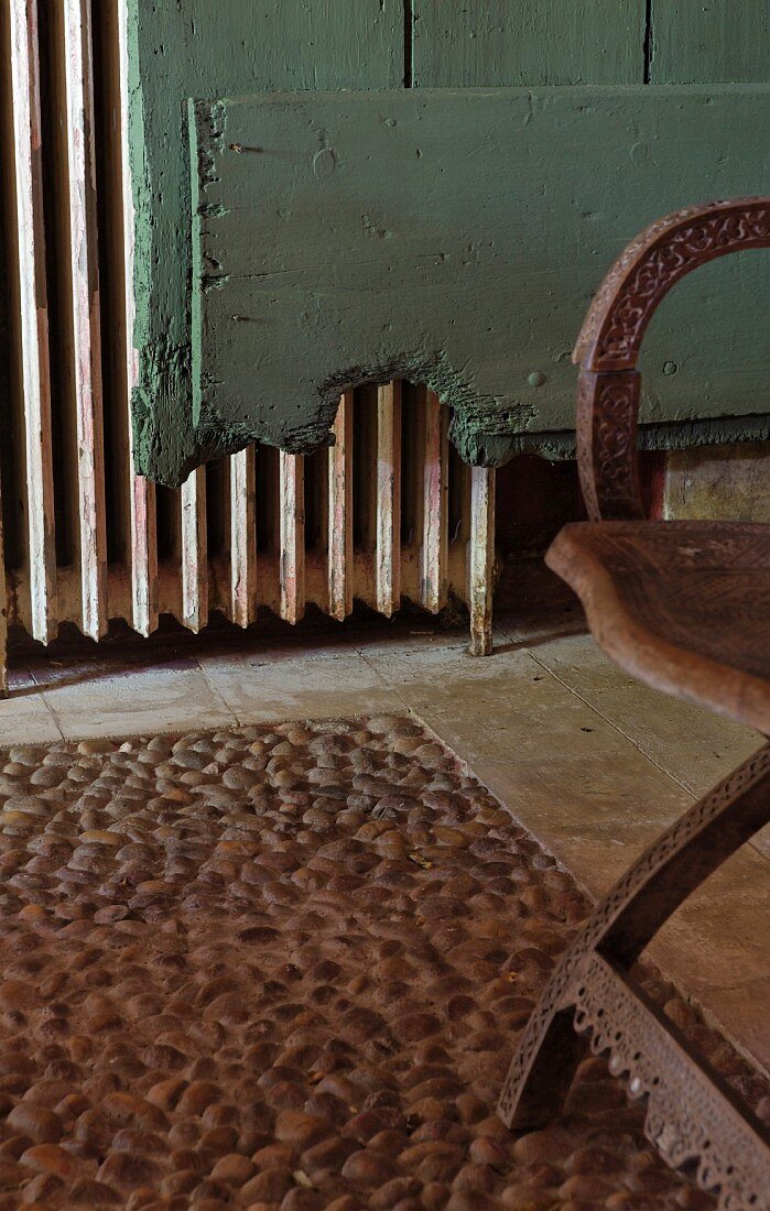 Steckkieselboden mit geschnitztem Stuhl vor türkisgrünem Vintagebrett und altem Heizkörper