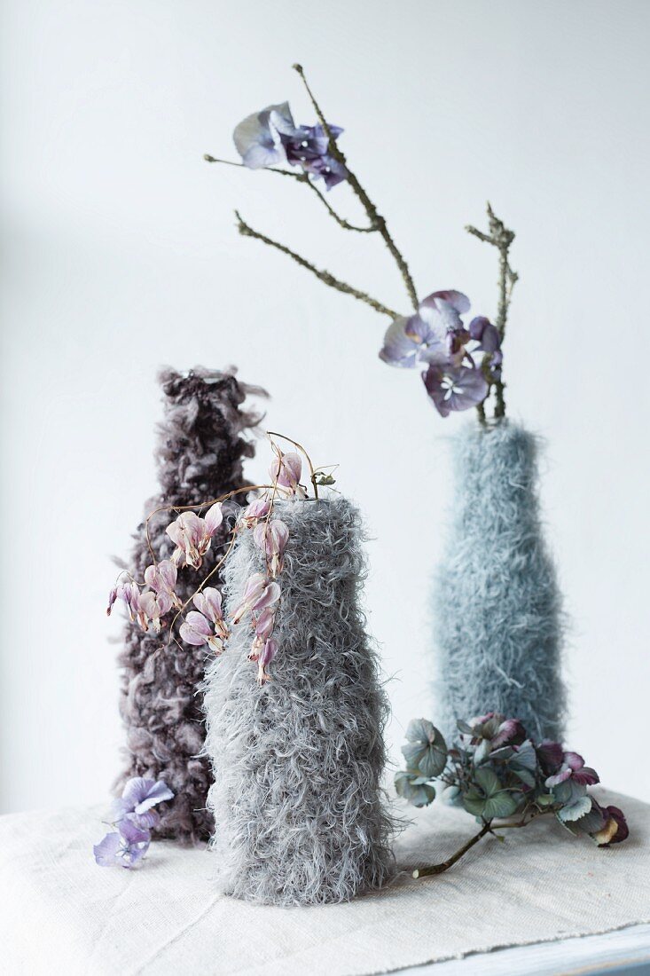 Vasen in gestrickten und gehäkelten Hüllen; getrocknete Blüten
