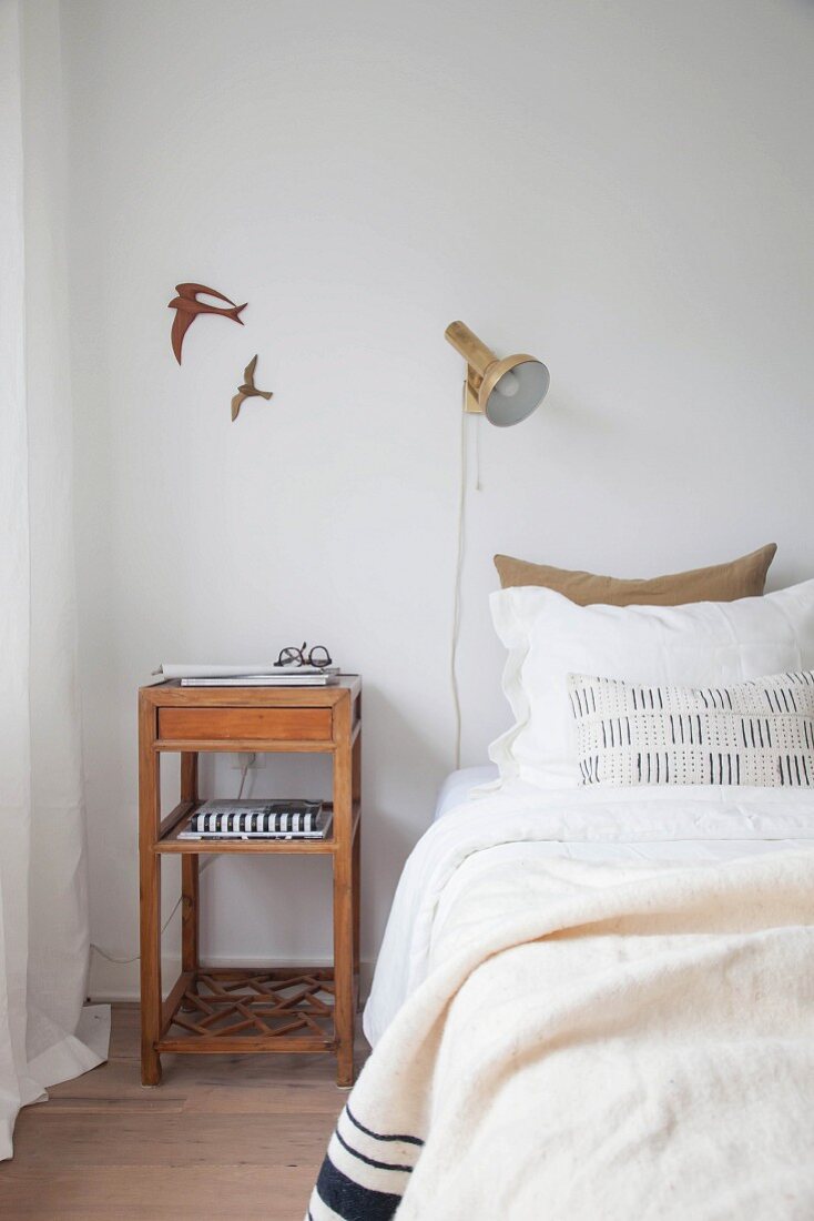 Schlichter Nachttisch aus Holz neben Bett, darüber Wanddeko mit Vogelmotiv und Wandleuchte