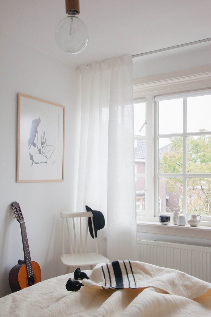 Weisser Holzstuhl neben Sprossenfenster und Gitarre in hellem Schlafzimmer mit ländlichem Flair