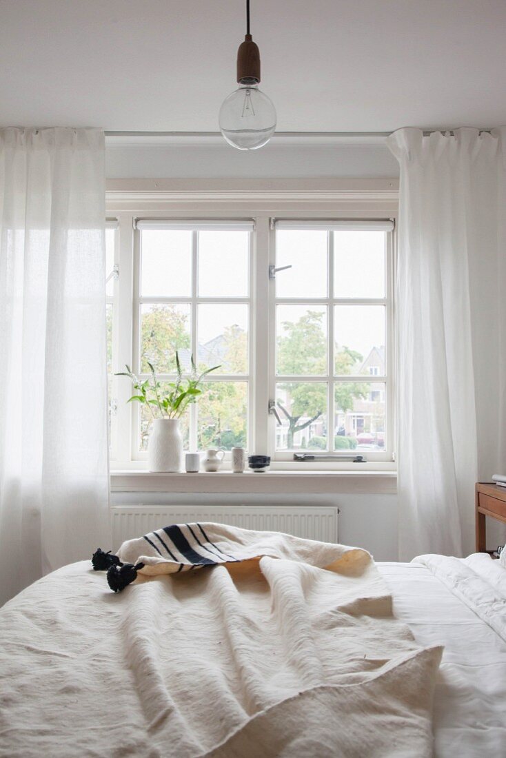 Off-white bedspread on bed below lattice window in rustic bedroom