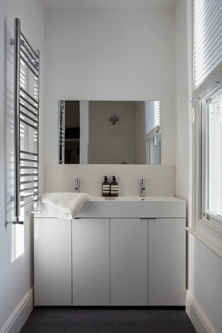 Twin washstand with white base unit and shiny towel rail in narrow bathroom with window