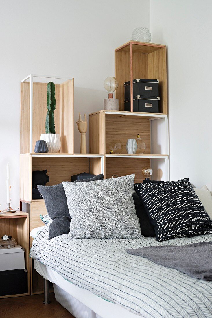 Bed with stacked shelving elements as headboard