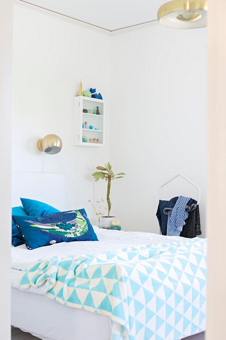 Blick ins Schlafzimmer auf Doppelbett mit weiss-blau gemusterter Tagesdecke und Kissen, oberhalb kugelförmige Wandleuchte