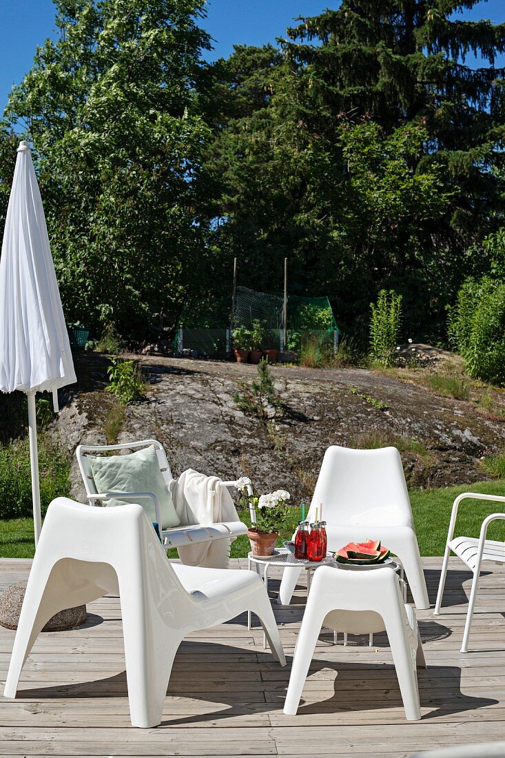 weiße Kunststoff Outdoor-Sessel auf sonnigem Holzdeck im Garten mit Felsen