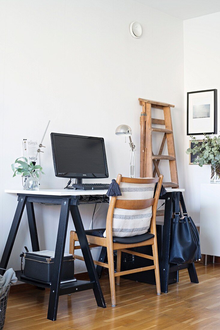 Holzstuhl und Arbeitstisch auf schwarzen Holzböcken in Zimmerecke mit minimalistischem Flair