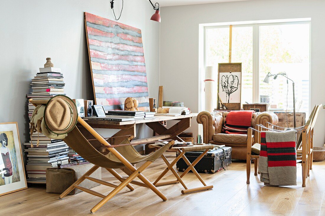 Klappbarer Sessel mit Holzgestell und passender Fusshocker in eklektischem Wohnzimmer mit Künstlerflair