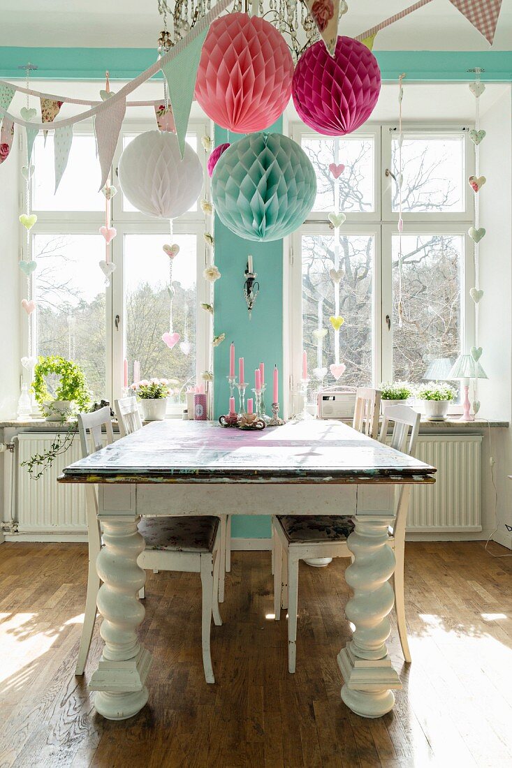 Wooden table with chunky turned legs in dining room romantically decorated with paper pompoms and bunting