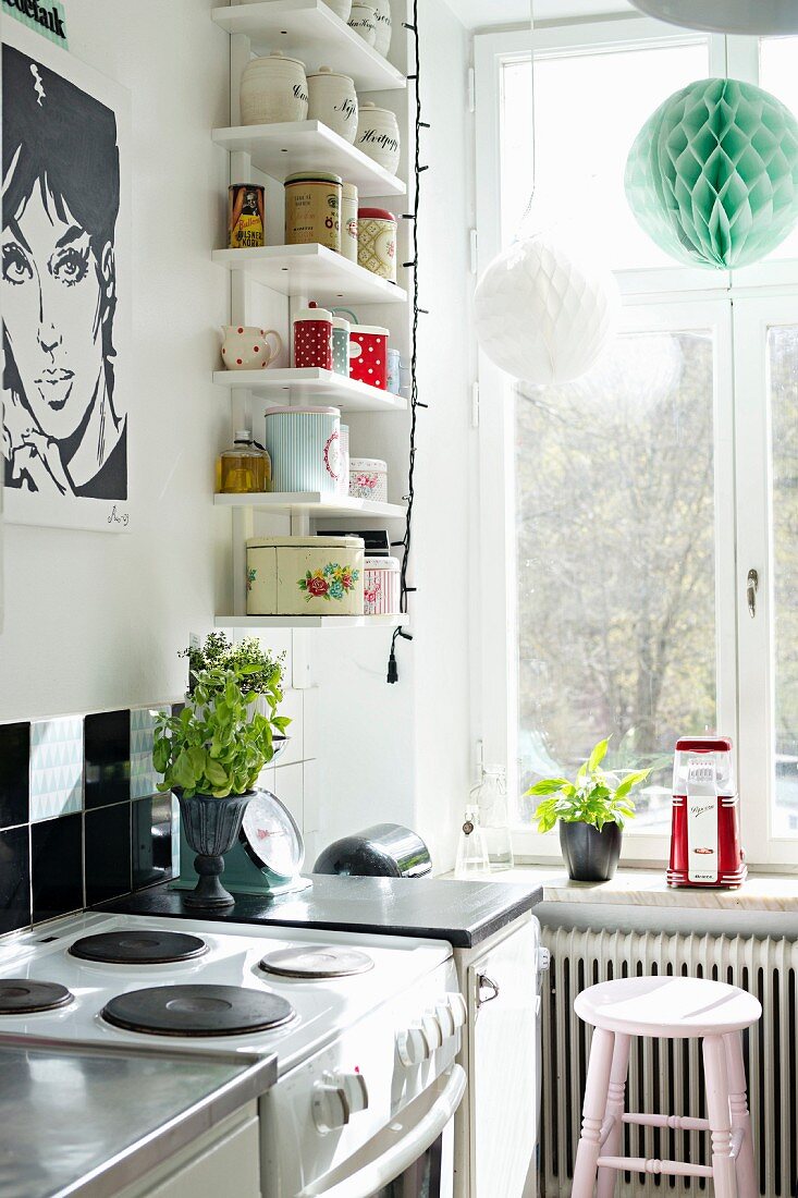 Black and white Pop-Art poster and vintage storage jars on white shelves in corner of kitchen