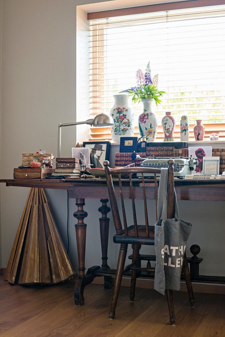 Antiker Holzstuhl vor vollem Schreibtisch mit gedrechselten Tischbeinen am Fenster, dekoriert mit Vasen