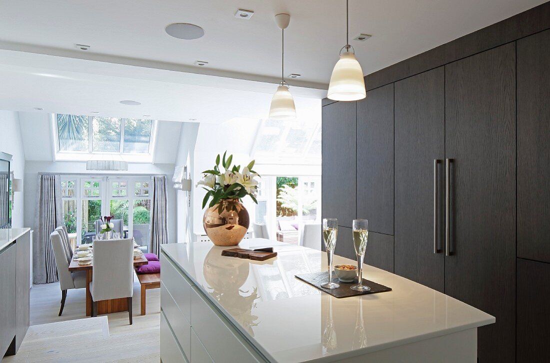 weiße Hochglanz-Kücheninsel und Einbauschrankwand mit dunkelbrauner Holzfront in eleganter, offener Küche