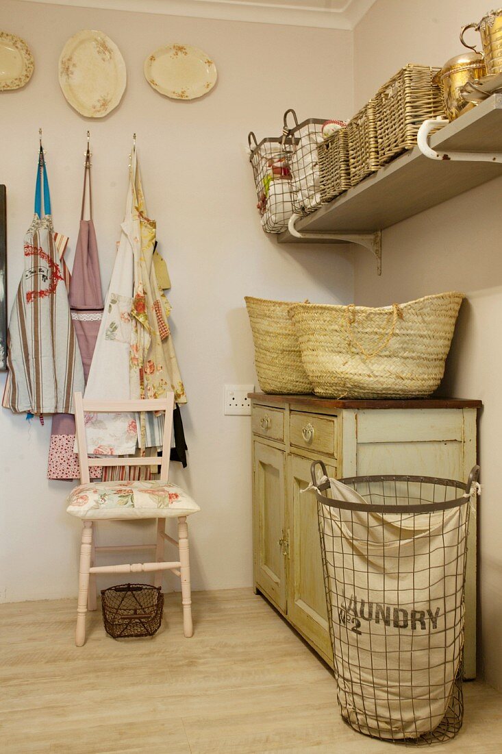 Wicker baskets on vintage cabinet, storage baskets on wall-mounted shelf, aprons and laundry basket in rustic room