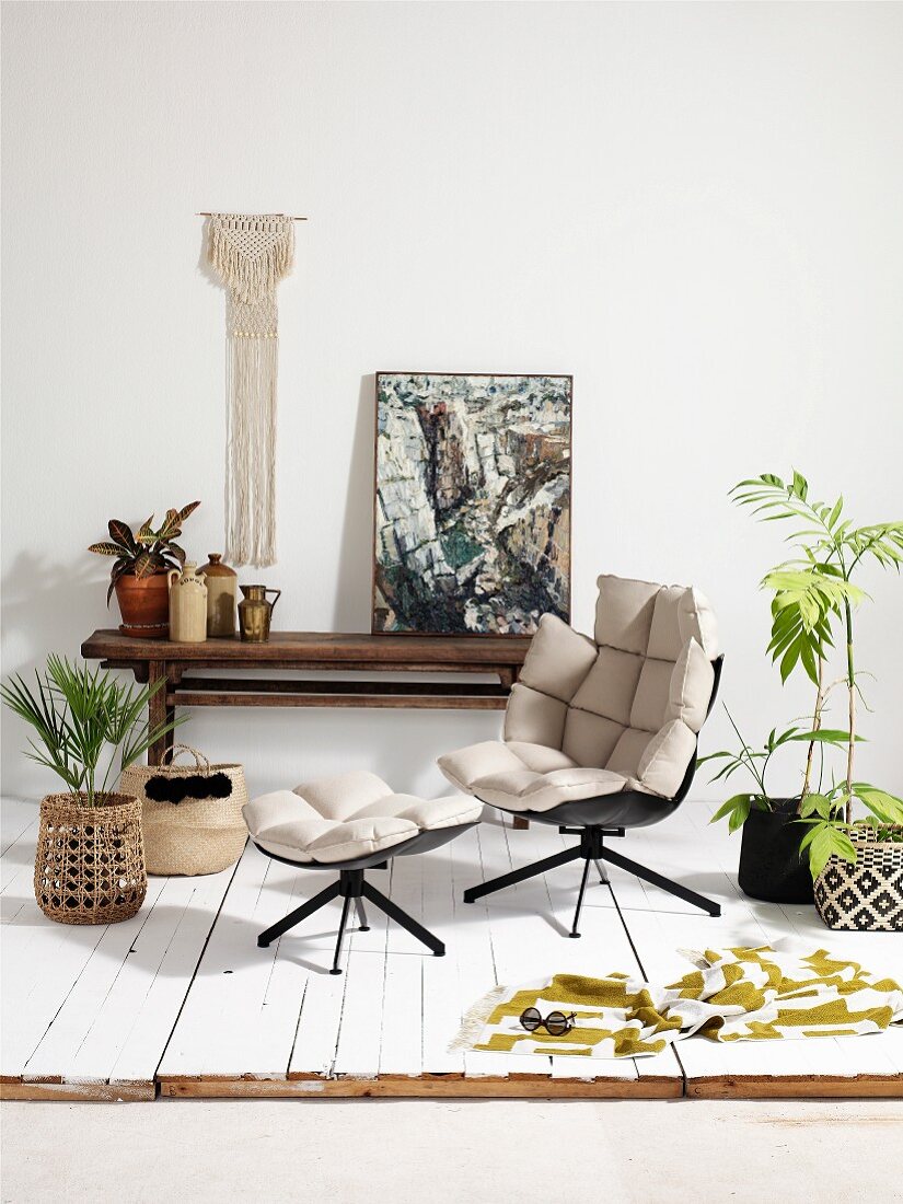 Designersessel und Fussschemel mit hellen Polstern, dazwischen Zimmerpflanzen
