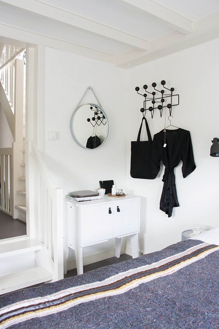View across grey blanket on bed to white cabinet next to doorway with wooden steps and classic black Hang-It-All coat rack