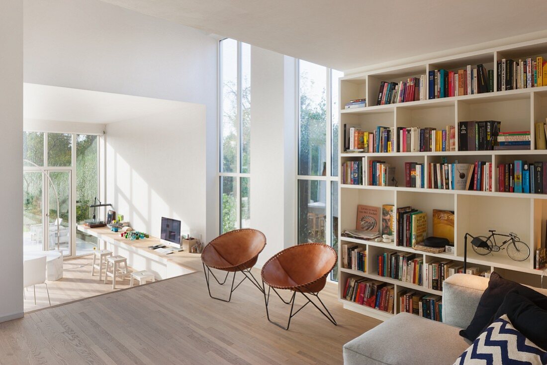 Wohnbereich mit hohen Fenstern und Bücherregalwand, Blick auf tieferen Thekenbereich
