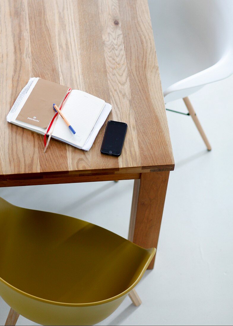Notizbuch und Smartphone auf Holztisch mit Schalenstühlen