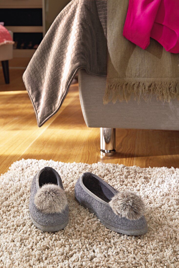 Hausschuhe mit Bommel auf Teppich, vor Bett mit verschiedenen Plaids