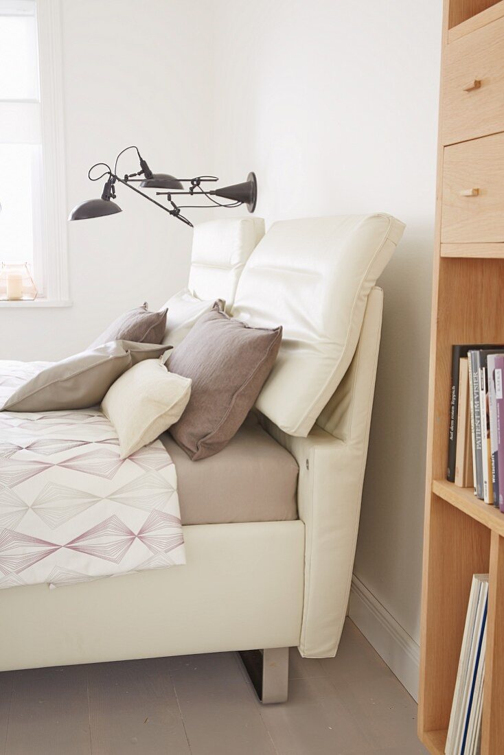A double bed with a light upholstered, movable headrest with a wall light in the background
