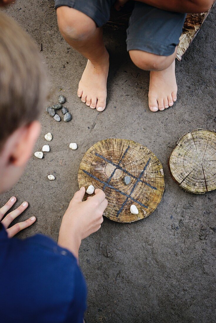 'Tic-Tac-Toe Spiel' mit Kindern; Kieselsteine und Baumscheibe als Spielbrett